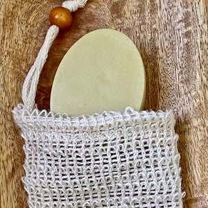 May include: A round, light green bar of soap in a white mesh bag with a brown wooden bead on the drawstring.