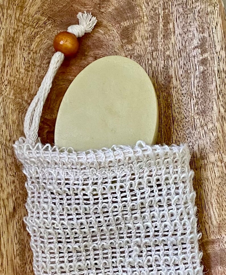 May include: A round, light green bar of soap in a white mesh bag with a brown wooden bead on the drawstring.