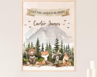 May include: A framed watercolor print featuring woodland animals: a bear, fox, raccoon, and deer. The print includes a mountain scene, pine trees, and the text "Let the Adventure Begin" and "Carter James". The artwork has a light wood frame.