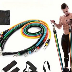 Può includere: Un set di fasce di resistenza colorate con manici neri e clip in metallo. Le fasce sono in vari colori, tra cui giallo, rosso, verde e blu. Sono inclusi anche una borsa per il trasporto nera e maniglie aggiuntive. Una persona sta usando le fasce sullo sfondo.
