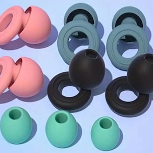 May include: An assortment of colorful, silicone objects in pink, teal, and black. The objects include ring-shaped pieces, spheres, and pieces with a hole in the center. The items are arranged on a light blue background.