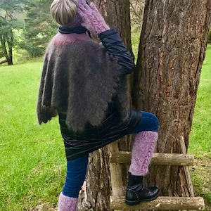 May include: A woman wearing a black jacket, a purple knitted shawl, and purple leg warmers stands on a wooden ladder in front of a tree.