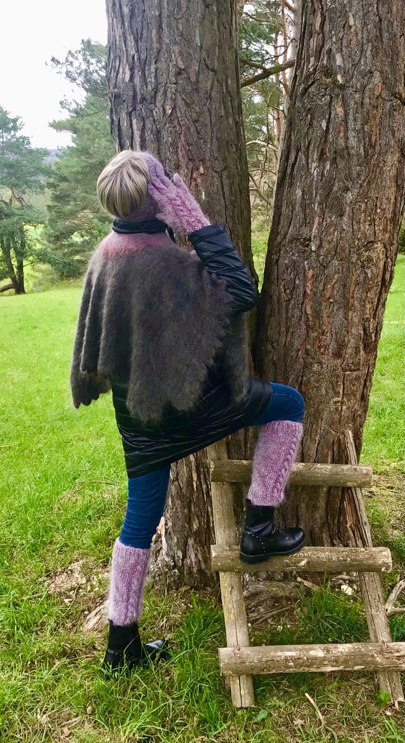 May include: A woman wearing a black jacket, a purple knitted shawl, and purple leg warmers stands on a wooden ladder in front of a tree.