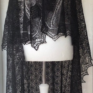 Puede incluir: Un chal de encaje negro con un patr&oacute;n delicado. El chal est&aacute; drapeado sobre un maniqu&iacute; blanco.