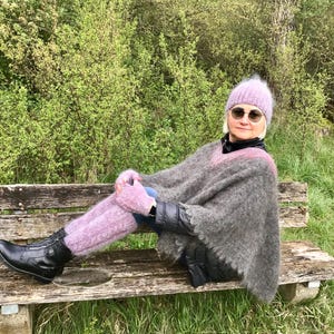 May include: A woman wearing a gray and black poncho, a pink fuzzy hat, and pink fuzzy leg warmers. She is sitting on a wooden bench in a forest setting.