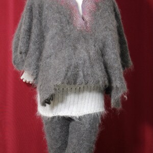 May include: A gray fuzzy knit poncho with a white knit band at the waist and a gray knit hat. The poncho has a V-neck and a subtle pink and purple design.