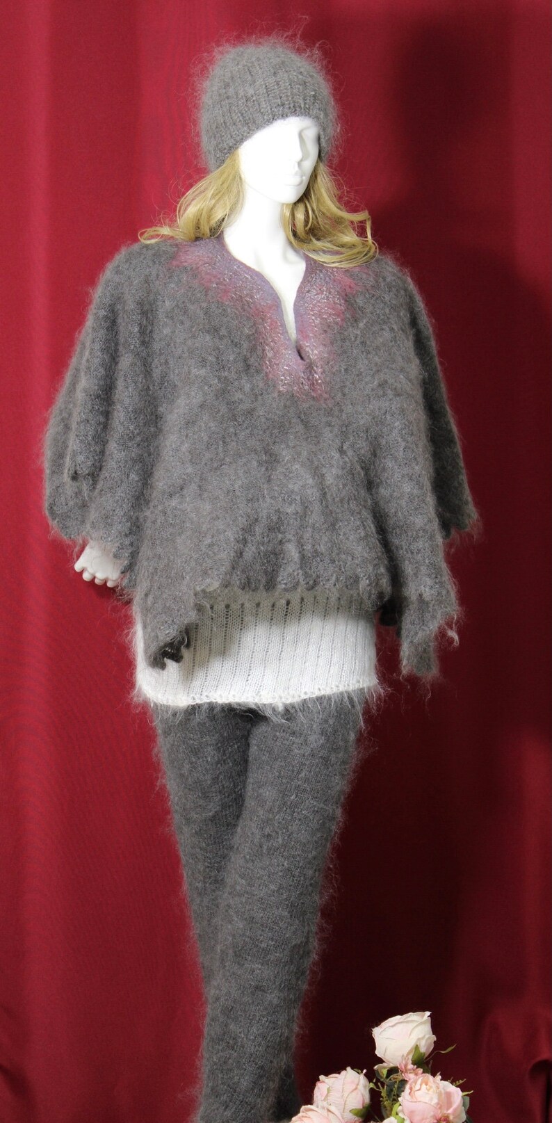 May include: A gray fuzzy knit poncho with a white knit band at the waist and a gray knit hat. The poncho has a V-neck and a subtle pink and purple design.