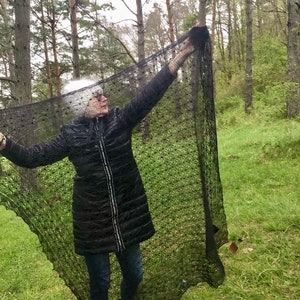 Puede incluir: Una persona con una chaqueta negra y pantalones vaqueros azules sostiene un chal de encaje negro con un patr&oacute;n de puntos. El chal est&aacute; drapeado sobre el cuerpo de la persona y se sostiene con los brazos. La persona est&aacute; de pie en un entorno boscoso.