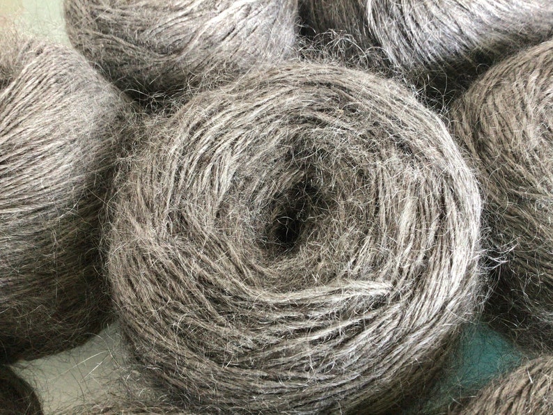 May include: Close-up of several spools of gray yarn. The yarn is tightly wound and has a fuzzy texture.