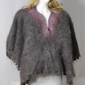 May include: A gray mohair poncho with a pink and purple trim. The poncho has a v-neck and is worn over a white knit top and gray leggings. The model is wearing a gray knit hat.