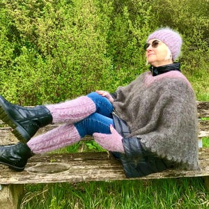 May include: A woman wearing a pink knit hat, sunglasses, a brown fuzzy poncho, and black boots sits on a wooden bench. She is wearing jeans and pink fuzzy socks.