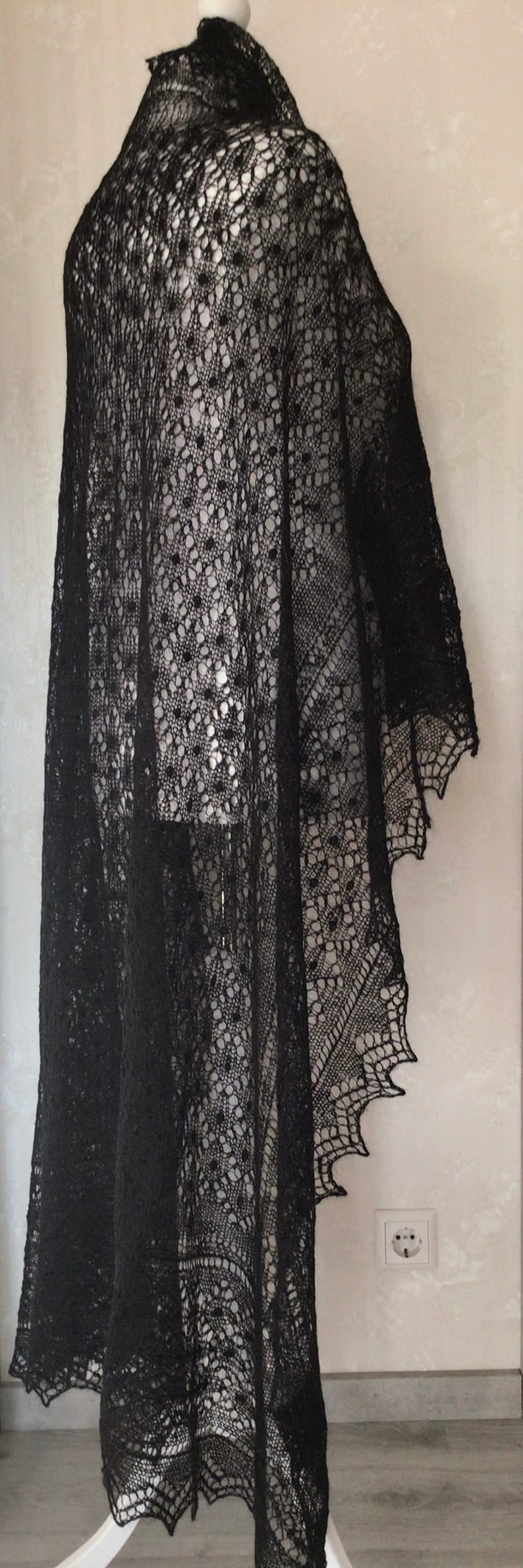 Puede incluir: Un chal de encaje negro con un patr&oacute;n delicado. El chal est&aacute; drapeado sobre un maniqu&iacute; blanco.