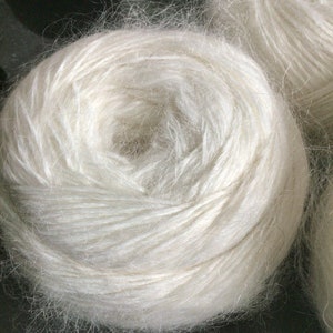 May include: A close-up of a white ball of yarn. The yarn is soft and fluffy, and it is wound into a tight coil.