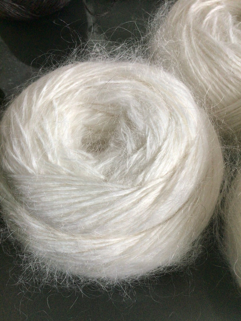 May include: A close-up of a white ball of yarn. The yarn is soft and fluffy, and it is wound into a tight coil.