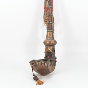 May include: A silver and brass ceremonial pipe with a long, curved stem and a decorative bowl. The pipe is adorned with turquoise and red stones and has a tassel hanging from the bowl.