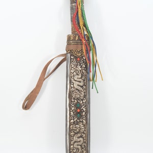 May include: A silver and gold scabbard with a dragon design and turquoise and red gemstones. The scabbard has a leather strap and a tassel of colorful cords.