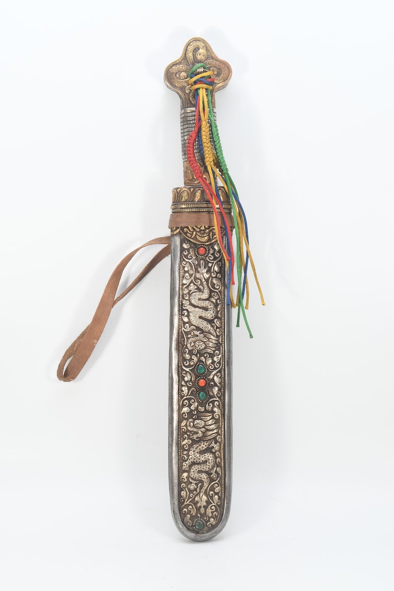 May include: A silver and gold scabbard with a dragon design and turquoise and red gemstones. The scabbard has a leather strap and a tassel of colorful cords.