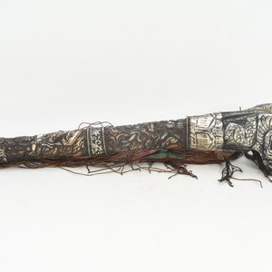 May include: A long, silver and brown ceremonial horn with intricate carvings and a tassel. The horn is decorated with silver bands and has a dragon-like head at the end.