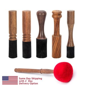 May include: Five wooden mallets with black suede heads and one red felt mallet with a wooden handle. The mallets are used for playing singing bowls.