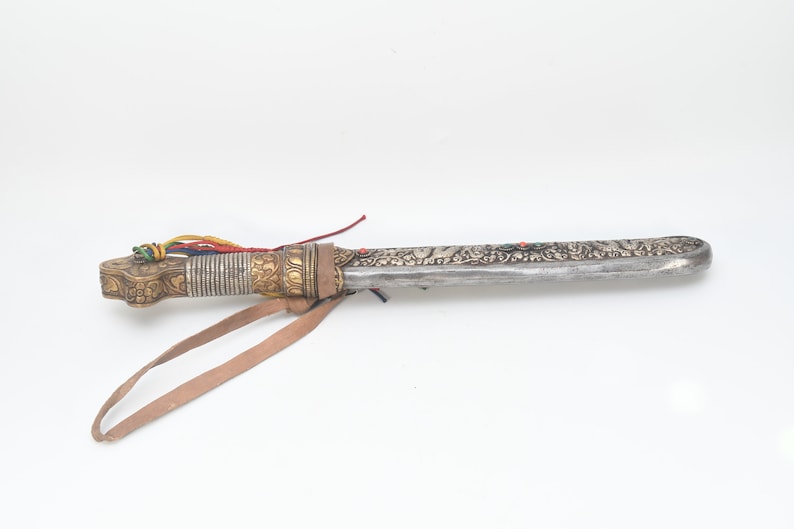 May include: A silver and gold decorated dagger with a leather strap and colorful tassels. The dagger has intricate floral designs and a sharp blade.