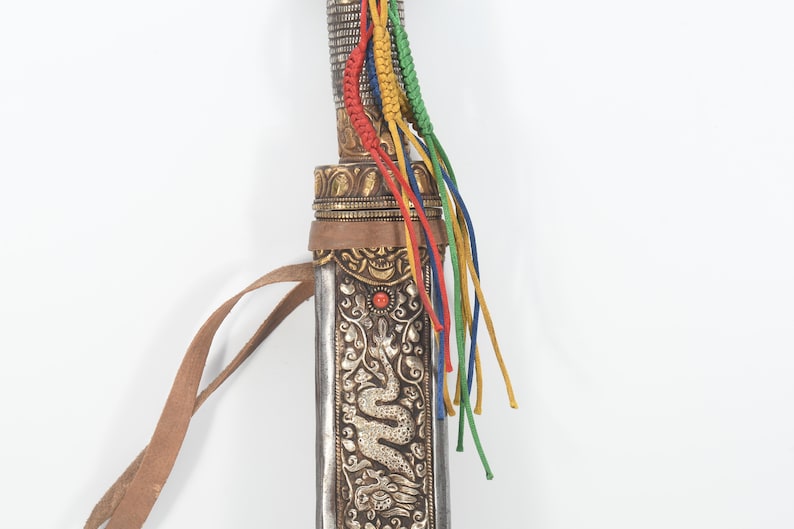 May include: A silver and gold decorated scabbard with a leather strap and colorful tassels. The scabbard has a dragon design and a red stone accent.