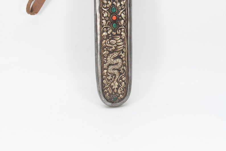 May include: A silver and gold scabbard with a dragon design and green and red gemstones. The scabbard is decorated with intricate floral patterns.