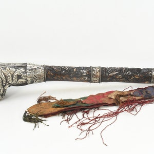 May include: An ornate, antique dagger with a silver handle featuring an animal head design. The dark wooden handle is intricately carved. A colorful sheath with tassels accompanies the dagger, showcasing a blend of red, green, and blue fabrics.
