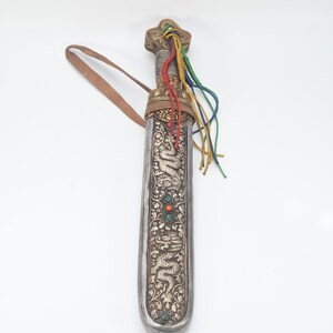 May include: A silver and gold scabbard with intricate dragon and floral designs. The scabbard has a leather strap and a colorful tassel.