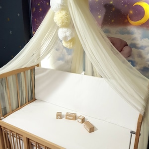 May include: A wooden crib with a white canopy and a white mattress. There are five wooden blocks on the mattress, with the words "6 Months", "Days", "Olivia" and a heart symbol.