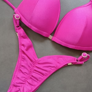 May include: A hot pink bikini with a halter top and a high-cut bottom. The bikini has crystal embellishments on the straps and sides.