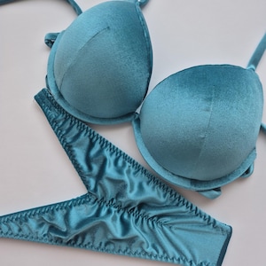 Puede incluir: Un conjunto de lencería turquesa que incluye un sujetador acolchado con tirantes ajustables y un tanga a juego. El sujetador y el tanga están hechos de un material suave y aterciopelado. El conjunto está diseñado para la comodidad y el estilo.
