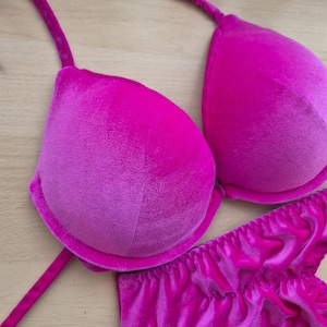 May include: A vibrant fuchsia velvet lingerie set. The set includes a padded bra with adjustable straps and a matching pair of ruffled panties. The fabric has a soft, plush texture. The bra cups are molded for shape and support.