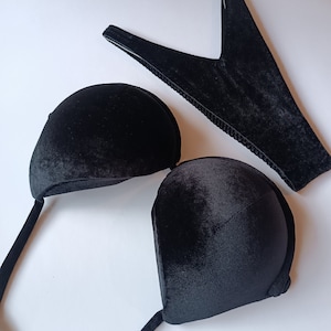 Pode incluir: Um conjunto de conchas de sutiã de veludo preto com alças ajustáveis e uma tanga combinando de veludo preto.