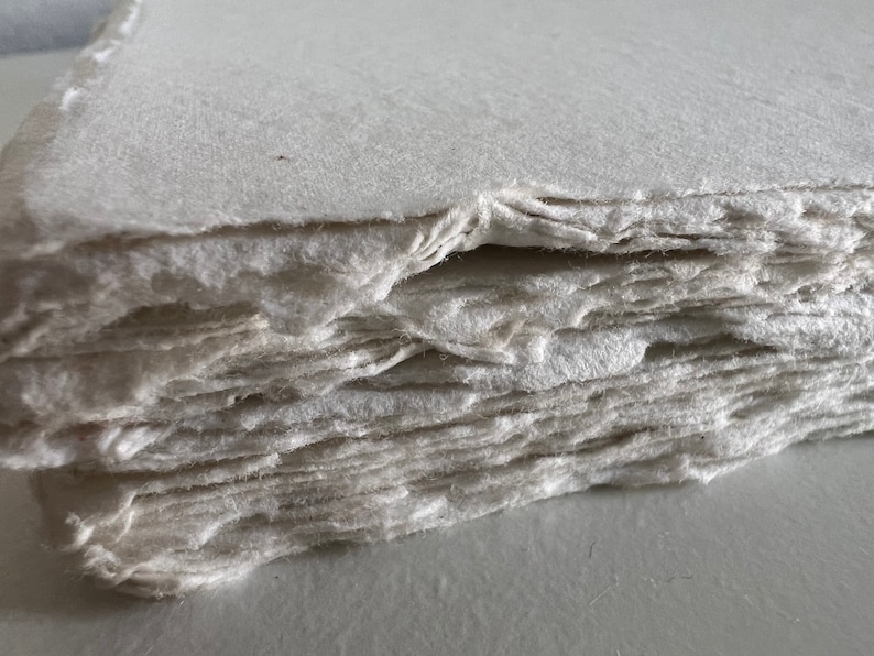 Peut inclure: Gros plan sur une pile de feuilles de papier fait main, montrant la surface rugueuse et textur&eacute;e et les bords irr&eacute;guliers.