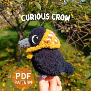 Könnte beinhalten: Ein dunkelblaues gehäkeltes Krähen-Stofftier mit grauem Schnabel, einem weiß-schwarzen Auge und einer gelben, strukturierten Kapuze mit weißen Akzenten. Der Text CURIOUS CROW und PDF PATTERN ist auf dem Bild des weichen Garnvogels zu sehen.