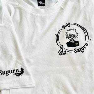 Op de afbeelding: Wit T-shirt met een zwart-witte grafische print van een personage met de tekst "Gojo Satoru" en een kleinere grafische print op de mouw die "Suguru" zegt.