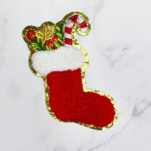 May include: A red and white Christmas stocking with gold glitter trim, filled with a candy cane and green and gold ornaments.