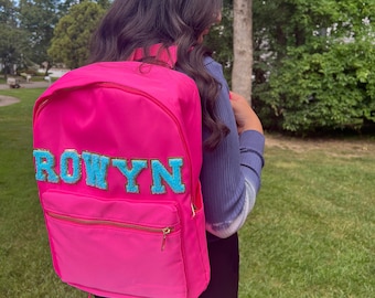 May include: A pink backpack with a blue and gold name patch that says "ROWYN".