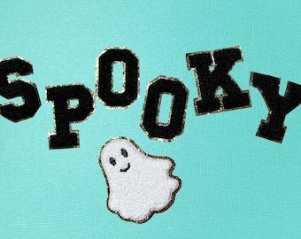 May include: A set of black varsity-style letter patches spelling the word SPOOKY with gold glitter borders, accompanied by a white ghost patch with a smiling face and gold glitter trim, all arranged against a solid light turquoise background.
