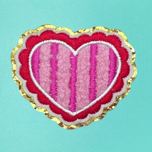 May include: A red and pink heart-shaped patch with white stitching and gold glitter around the edges.