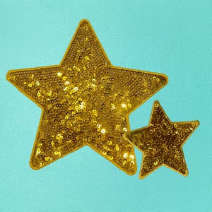 May include: Two gold sequined stars on a turquoise background. The larger star is on top of the smaller star.