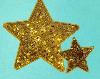 May include: Two gold sequined stars on a turquoise background. The larger star is on top of the smaller star.