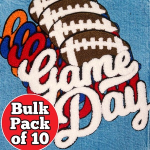 May include: A blue denim jacket with a white, red, and orange embroidered patch that says "Game Day" with a stack of brown footballs behind the text. The patch is surrounded by a red circle with the text "Bulk Pack of 10".