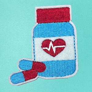 May include: Embroidered patch of a blue pill bottle with a red lid and a red heart with a white EKG line inside. Two red and blue pills are next to the bottle.