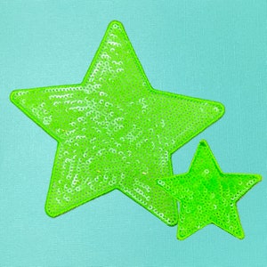 May include: Two green sequined stars on a light blue background. The larger star is on top of the smaller star.