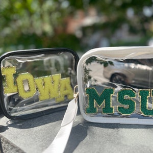 May include: Two clear plastic tote bags with black and white straps. The bag on the left has a yellow "IOWA" patch and the bag on the right has a green "MSU" patch.