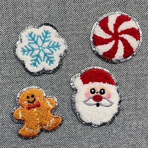 May include: Four Christmas-themed fabric patches. Includes a white snowflake with blue accents, a red and white peppermint candy, a gingerbread man with a red bow tie, and a Santa Claus face with a red hat.