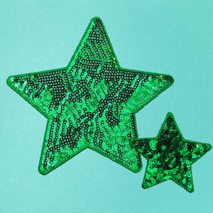 May include: Two green sparkly star-shaped patches on a light blue background.