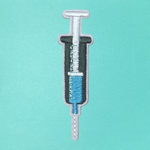 May include: A blue and white embroidered iron-on patch of a syringe with a needle.