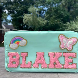 May include: A light green zippered pouch with a pink butterfly, rainbow, and the name "BLAKE" in pink fluffy letters.